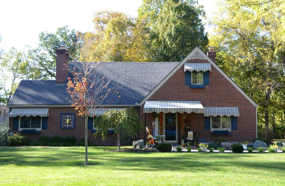 A large mature shade tree standing over a house and lawn